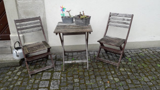 Zwei Stühle und ein kleiner Tisch im Freien als Bild für ein Gespräch