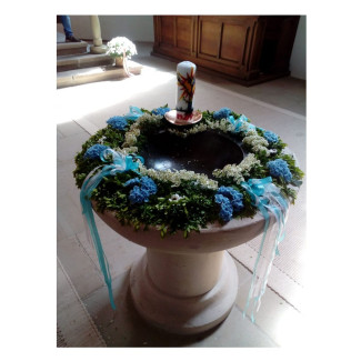 Taufstein mit einem Kranz aus blauen und weißen Blüten