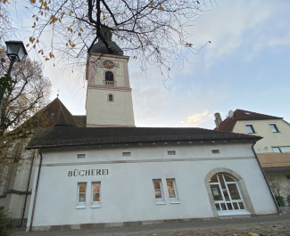 Gebäude der Bücherei mit Schriftzug, dahinter der Kirchturm